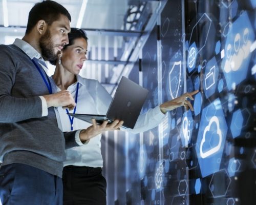 Male IT Specialist Holds Laptop and Discusses Work with Female Server Technician. They're Standing in Data Center, Rack Server Cabinet with Cloud Server Icon and Visualization.